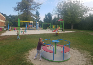 Dziewczynka przy huśtawce, chłopczyk spacerujący po trawie.