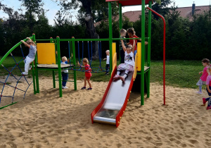 Dzieci bawią się na przedszkolnym placu zabaw - zjeżdżają na zjeżdżalni, wspinaja się po sznurach i drabinkach