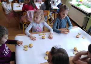 Dzieci siedzą przy stolikach, w oczekiwaniu na dekorowanie ciasteczek