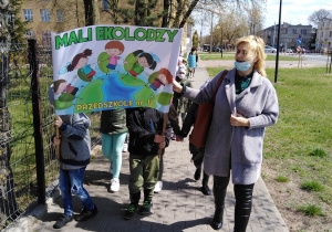 Dzieci z wychowawczynią niosą transparent "Mali Ekolodzy" i idą ulicami naszego miasta