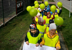Dzieci z plakatem i zielonymi balonami idą ulicami miasta