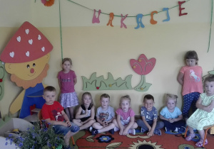 Dzieci siedzą przed napisem "wakacje"