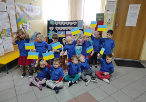 Dzieci z grupy Muchomorki na tle darów, w dłoniach trzymają małe flagi Ukrainy