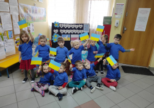 Dzieci z grupy Muchomorki na tle darów, w dłoniach trzymają małe flagi Ukrainy