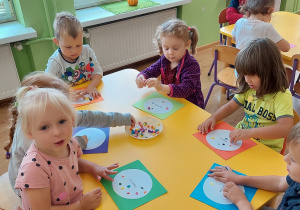 Dzieci przy stolikach ozdabiają kropki za pomocą plasteliny