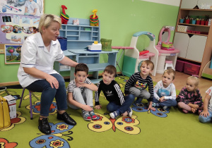 Dzieci siedzą na dywanie i słuchają pielęgniarki
