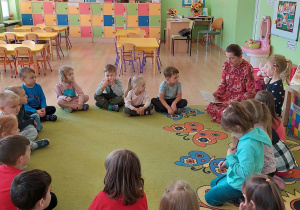 Dzieci siedzą w kole na dywanie i słuchają opowieści