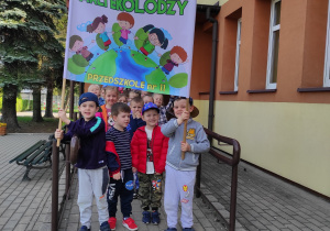 Dzieci stoją przed przedszkolem trzymając transparent