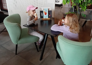 Dziewczynki siedzą przy stoliku i jedzą lody