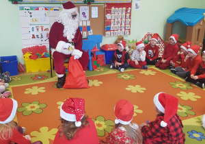 Dzieci siedzą na dywanie i rozmawiają z Mikołajem