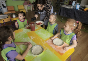 Dziewczynki z prowadzącą nakładają sos na pizzę