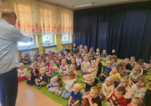 Dzieci siedzą na dywanie i oglądają występ