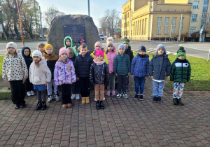 Dzieci stoją w postawie szacunku przed pomnikiem harcerzy