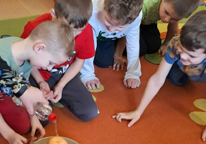 dzieci obserwują zabawioną na pomarańczowo reakcję sody z octem.