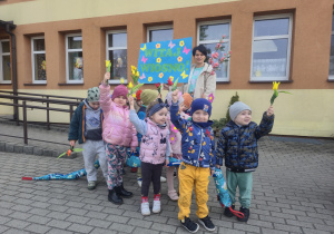 Dzieci stoją przed przedszkolem z transparentem "Witaj Wiosno"