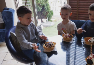 Dzieci siedzą przy kawiarnianych stolikach z deserkami lodowymi