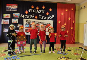Dzieci przebrane za ogniki stoją na środku sali ze strażakiem.