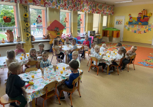 Dzieci siedzą przy stolikach i jedzą poczęstunek