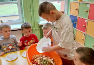 Chłopiec miesza pokrojone jabłka, gruszki, winogrona, banany, itp.