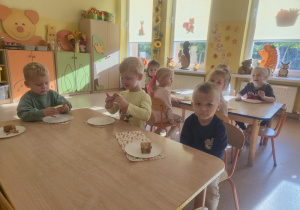 Dzieci siedzą przy stołach i jedzą ciasto
